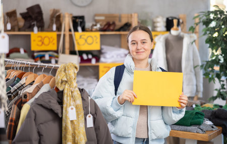 Happy teen girl holding sign saying Sale for Black Friday sale of winter clothing collection...