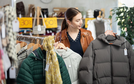 Attractive female customer chooses autumn down jacket in clothing boutique. Saleの写真素材