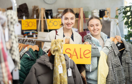 Happy family holding sign saying Sale for winter clothing collection standing in interior of clothing boutiqueの写真素材