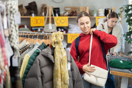 Happy teenage girl choosing ladies handbag in clothing shop with large assortment