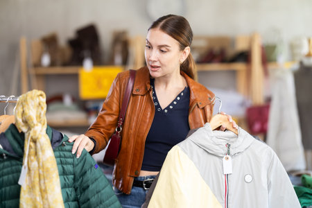 Attractive female customer chooses autumn down jacket in clothing boutique. Black Friday sale