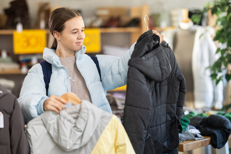 Teenager girl standing in clothing shop and looking new down jacket made of high-quality material. Shopping and seasonal sales concept, autumn-winter seasonの写真素材
