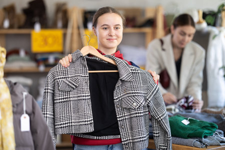 Positive teen girl choosing winter coat in clothing storeの写真素材