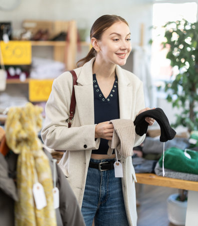 Focused fashionable young lady choosing warm gloves for autumn-winter season in clothing shop. Black Friday sale of winter clothing collectionの写真素材
