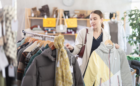 Adult woman chooses down jacket in clothing storeの写真素材