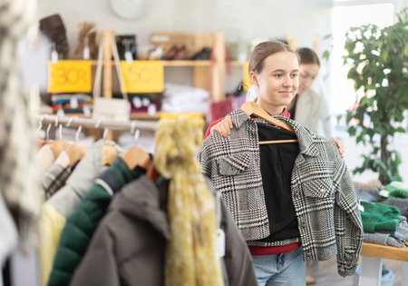 Positive teen girl choosing winter coat in clothing storeの写真素材