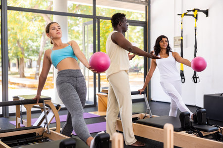 Women exercising pilates with male trainer in gym