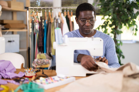 Working in sewing workshop - male tailor working at sewing machine making stitches on fabric
