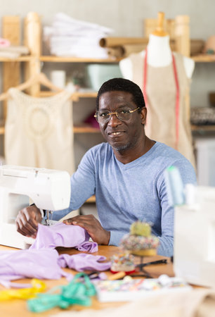 African American man tailor sews clothes in sewing machine.の写真素材