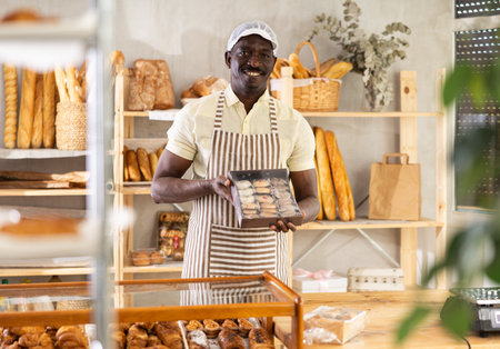 Male baker worker sells cookie, shows many productsの写真素材