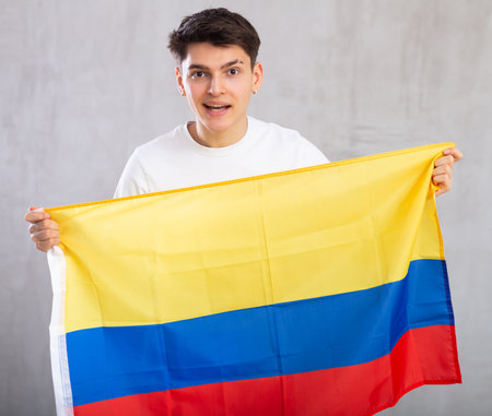 Happy young man holding flag of Colombia against unicoloured backgroundの写真素材