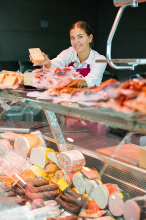 Cheerful young salesgirl offering piece of vacuum-packed fresh cheeseの写真素材