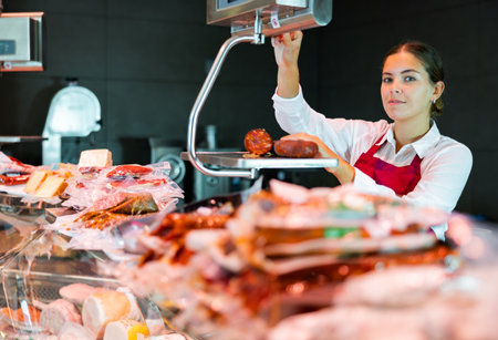 Female seller weighing sausage on scale in butcher shopの写真素材