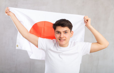 Happy young man holding flag of Japan against unicoloured backgroundの写真素材