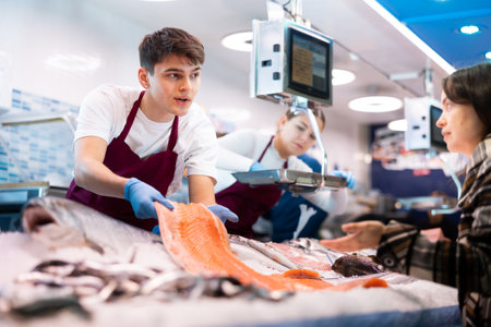 Portrait of man offering female customer fresh fish at seafood shopの写真素材