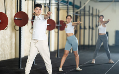 Young guy, together with other athletes, does a warm-up using a long stick in gymの写真素材
