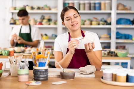 Woman painting with brush on handmade clay cupの写真素材