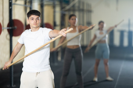 Young guy, together with other athletes, does a warm-up using a long stick in gymの写真素材