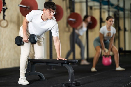 Young guy training with dumbbells on benchの写真素材