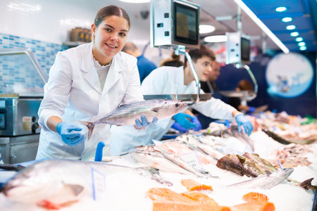 Positive saleswoman demonstrating bonito fish in fish storeの写真素材