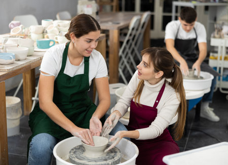 Woman working with pottery wheel and master giving instructionsの写真素材