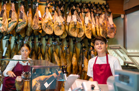 Positive young man and woman selling spanish jamon at counterの写真素材
