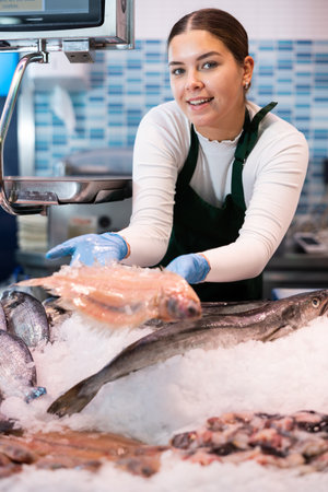 Female seller shows hands fish on counter in supermarketの写真素材