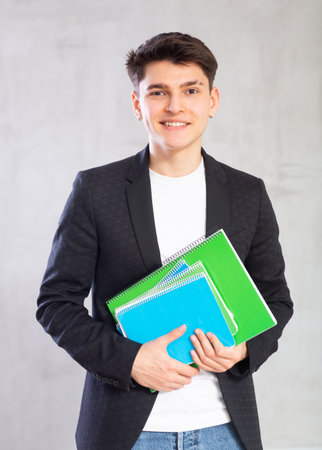 Smiling young guy holding stack of notebooksの写真素材