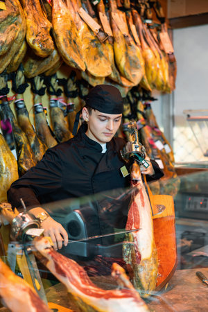 Young salesman in black uniform with leg of jamon in hands imitating playing celloの写真素材