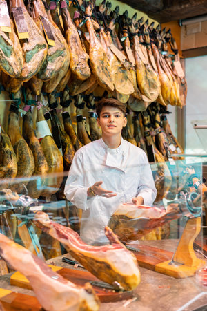 Young salesman in white uniform recommending iberian ham in meat shopの写真素材