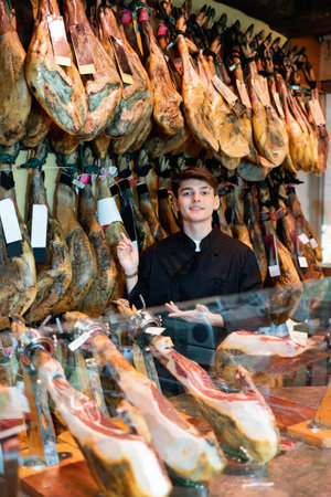 Young salesman in black uniform recommending iberian ham in meat shopの写真素材