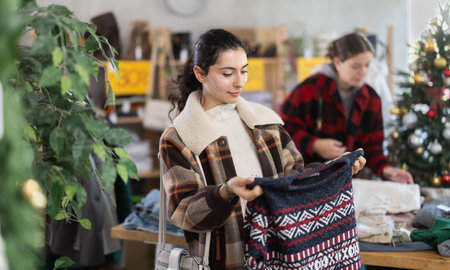 Positive young Armenian girl choosing sweater in clothing store