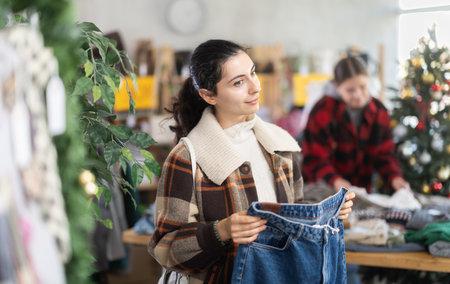 Armenian woman stands against the background of a Christmas tree and chooses denim pantsの写真素材