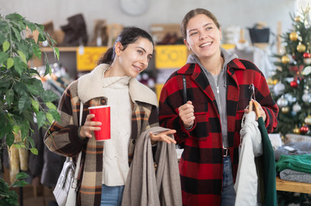 Two girls with cup of coffee talking during shopping in clothing storeの写真素材