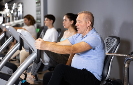 Elderly man, along with other people, is engaged on an exercise bike in gymの写真素材