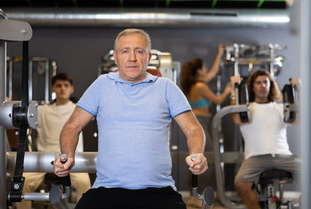 Elderly active man exercising on a simulator in modern gymの写真素材