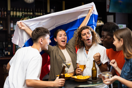 Cheerful international soccer football fans waving Russian flag and drinking beer, eating chips in the sport barの写真素材