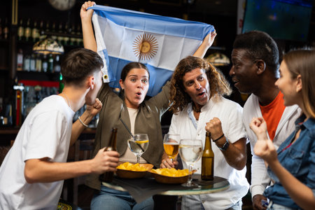 Happy international fans waving the flag of Argentina, drinking beer, watching football match in the barの写真素材