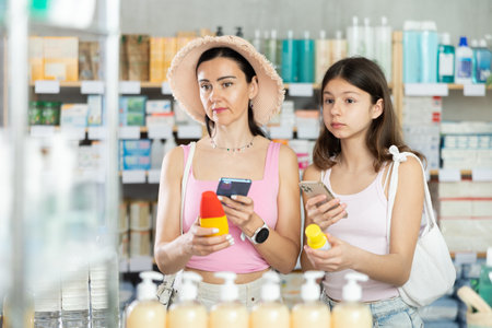 Interested mother and daughter customers preparing for summer season, holding and examines label and content of mosquito repellent.の写真素材