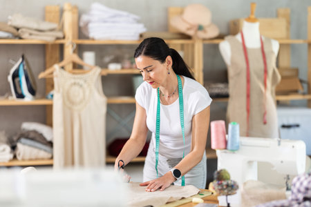 Woman seamstress cuts fabric on cutting tableの写真素材