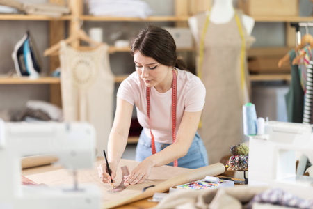 Girl tailor draws pattern on a sheet of paper in sewing workshop