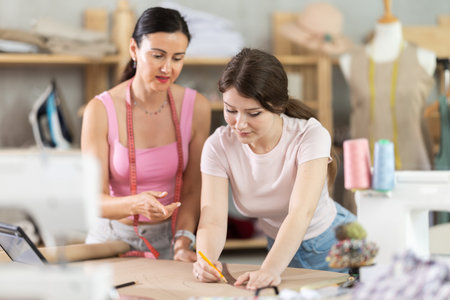 Manager of sewing workshop teaches a young girl seamstress to draw using patternsの写真素材