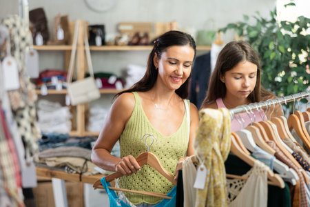 Positive mother and teenage daughter choosing something for summer in clothing storeの写真素材