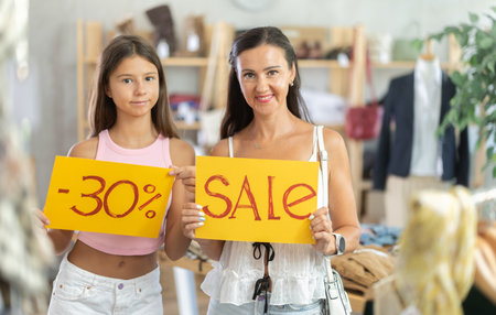 Mother with teenage daughter holding bright discount signs in clothing storeの写真素材