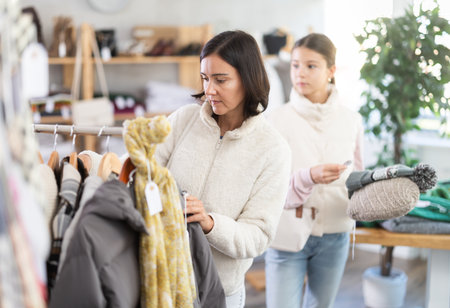 Mother and teen daughter looks at products in store and selects coat or jacket for childの写真素材