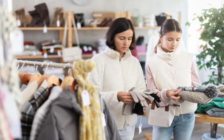 Mother and teen daughter looks at products in store and selects winter hat and glovesの写真素材