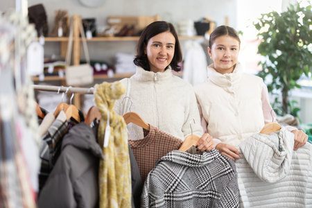 Mother and teen daughter looks at products in store and selects coat or jacket.の写真素材
