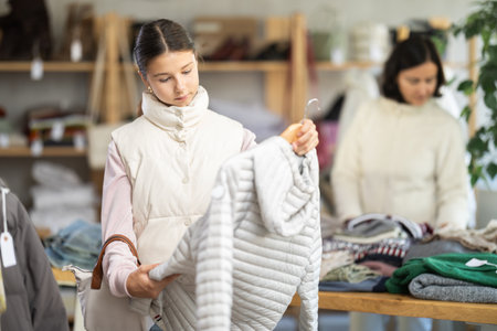 Teen girl looks at products in store and selects coat or jacket. Family shoppingの写真素材