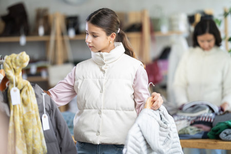Teen girl looks at products in store and selects coat or jacket. Family shoppingの写真素材