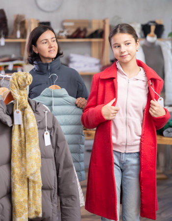 Teenage girl with her mother try on coat in storeの写真素材